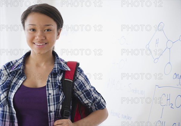 Smiling mixed race teenage girl standing next to whiteboard in science class