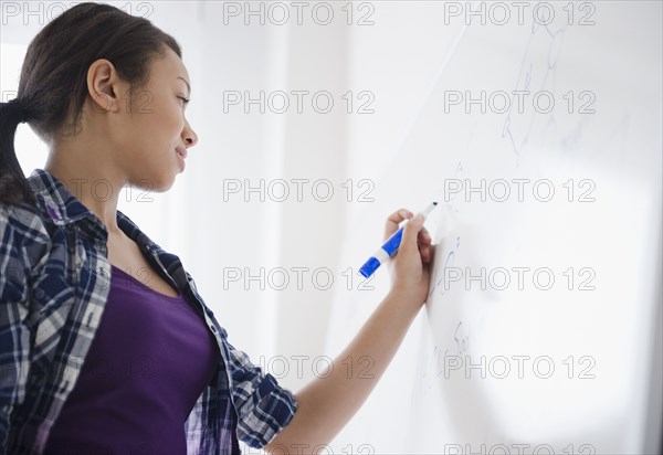 Mixed race teenage girl writing on whiteboard in classroom