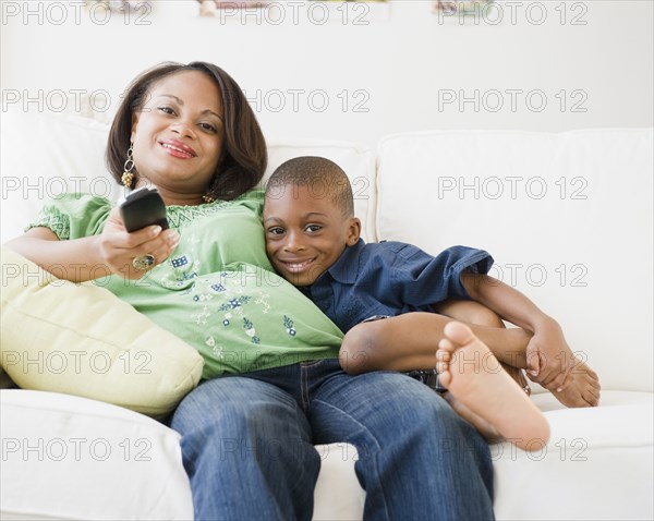 Black mother and son watching TV on living room sofa