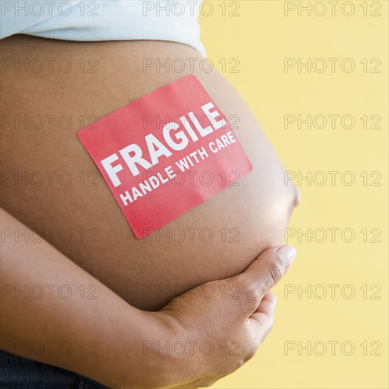Close up of 'Fragile' sticker on pregnant Black woman's stomach