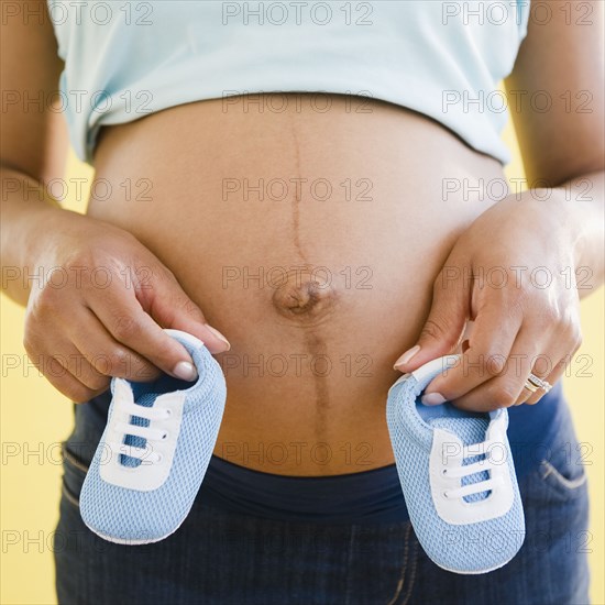 Close up of pregnant Black woman holding blue baby booties to stomach