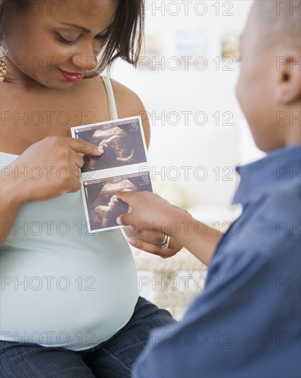 Pregnant Black mother showing sonogram to son