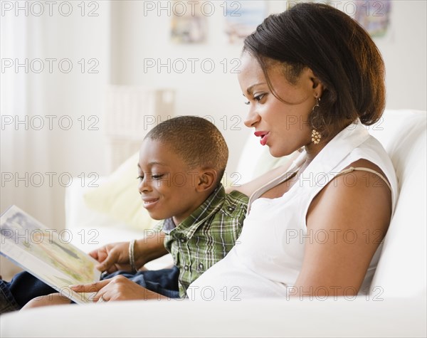 Black mother and son reading book on living room sofa