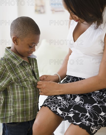 Black mother buttoning son's shirt