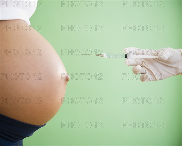 Gloved hand pointing needle at pregnant woman's stomach