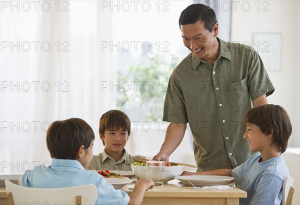 Father serving dinner to sons at table