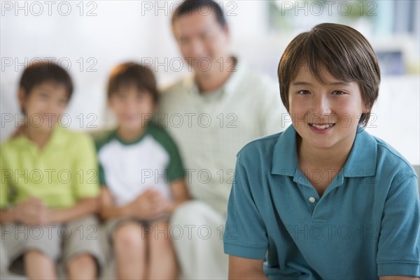 Smiling boy in living room with father and brothers in background