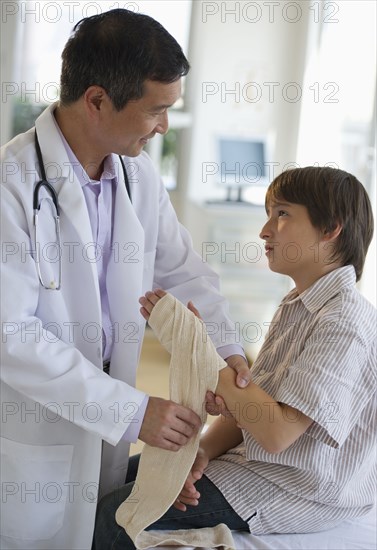 Doctor wrapping boy's hand with bandage in examination room