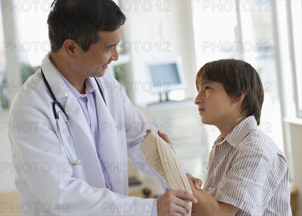 Doctor wrapping boy's hand with bandage in examination room