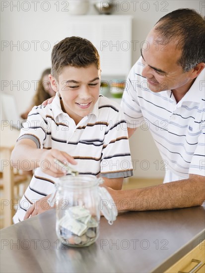 Hispanic father watching son put money into jar