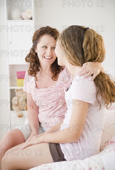 Hispanic mother sitting on bed hugging daughter