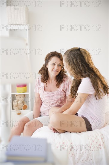 Hispanic mother sitting on bed talking to daughter