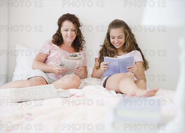 Hispanic mother and daughter reading together in bed