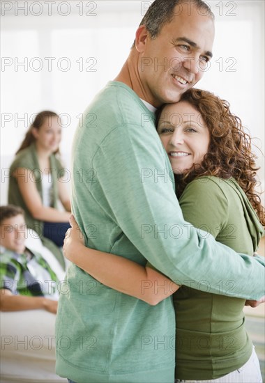 Hispanic husband and wife hugging with family in background