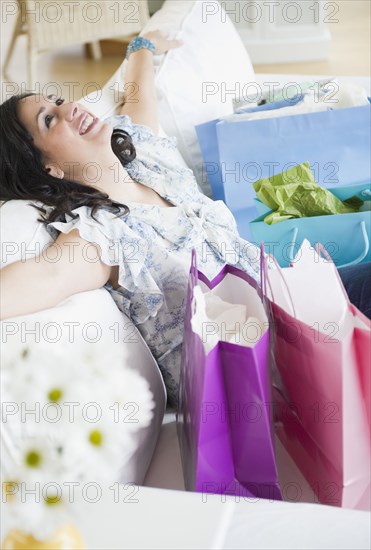 Smiling Hispanic woman sitting on sofa with shopping bags