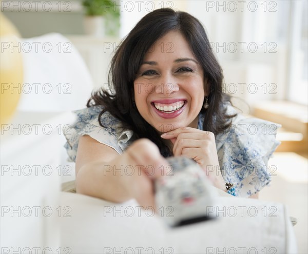 Smiling Hispanic woman changing channel with remote control