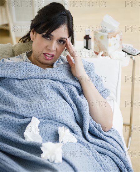 Sick Hispanic woman laying on sofa under blanket