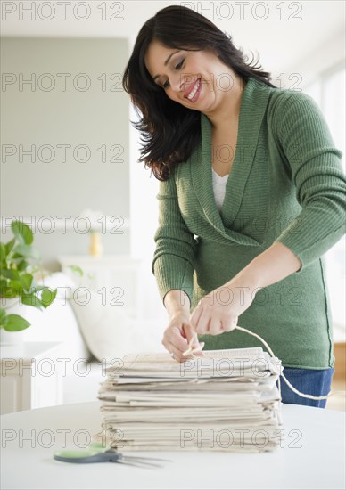 Smiling Hispanic woman trying newspapers in bundle
