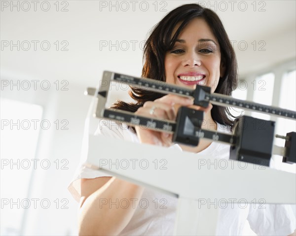 Smiling Hispanic woman weighing herself on scale