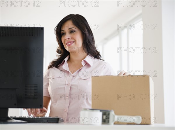 Smiling Hispanic woman with cardboard box using computer