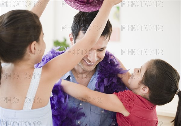 Daughters dressing father in feather boa and hat