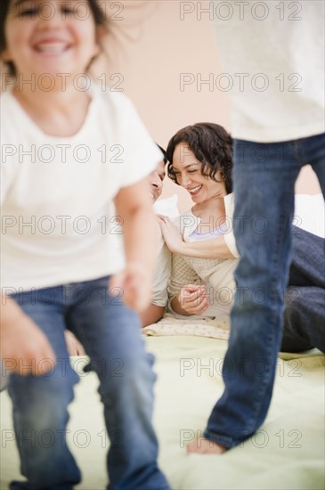 Parents watching daughters jumping on bed