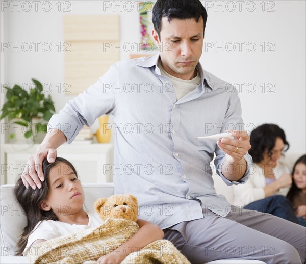 Father taking sick daughter's temperature with thermometer