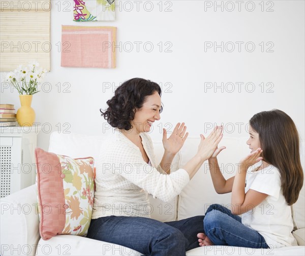 Mother playing hand game with daughter on sofa