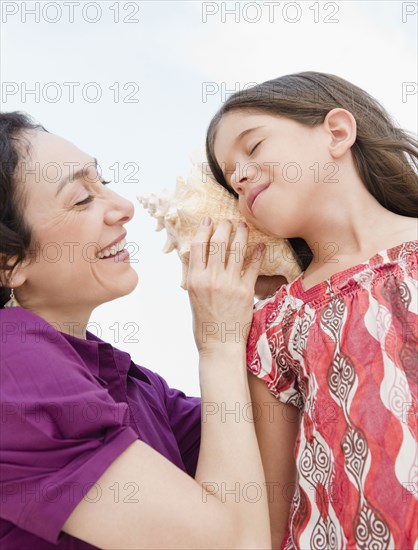 Mother holding seashell to daughter's ear