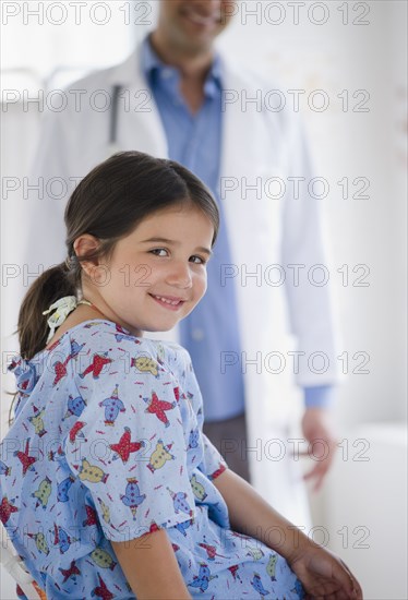 Smiling mixed race girl in examination room with doctor in background