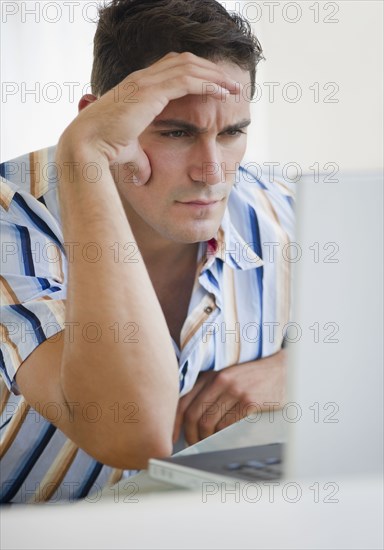 Frustrated mixed race businessman frowning at laptop