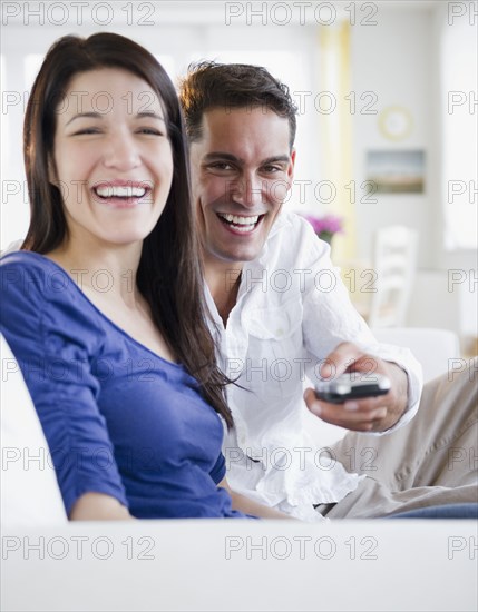 Mixed race man with remote control watching television with wife