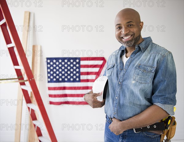 African American construction worker holding hard-hat near American flag