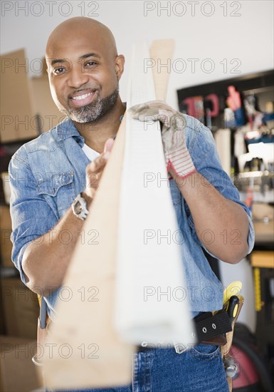 African American construction worker carrying lumber