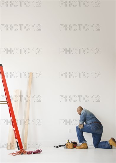 African American construction worker kneeling to look at wall