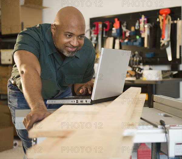 African American carpenter using laptop in workshop