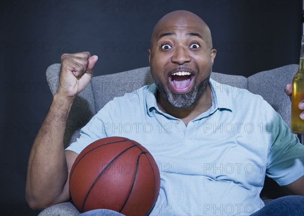 African American man drinking beer and watching basketball on television