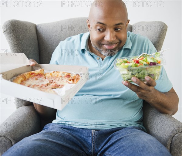 African American deciding between salad and pizza