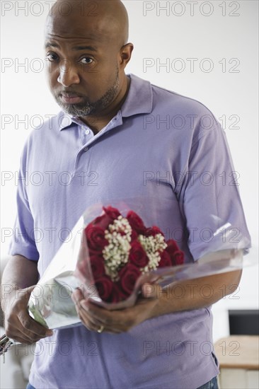 Sad African American man holding bouquet of roses