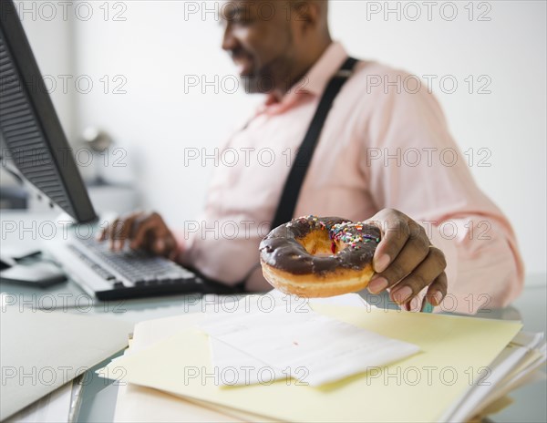 African American businessman eating donut at desk