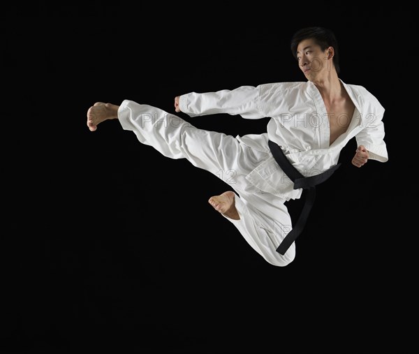 Asian male karate black belt kicking in air