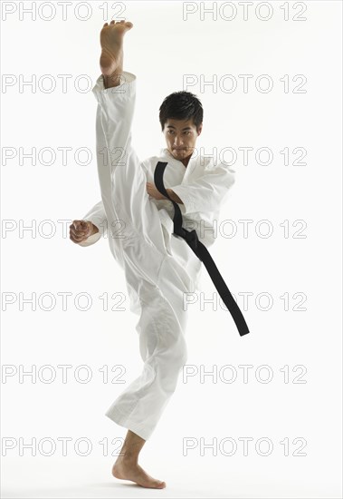 Asian male karate black belt kicking in air