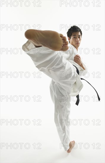 Asian male karate black belt kicking in air