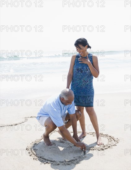 Black man drawing heart on beach for wife