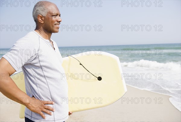 Black man holding body board on beach