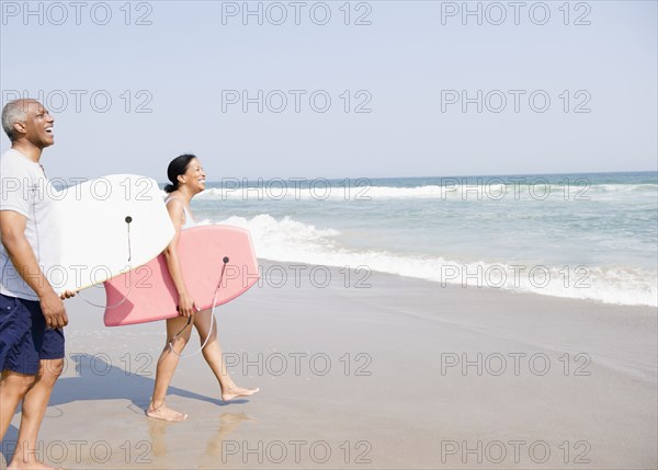 Black couple holding body boards on beach