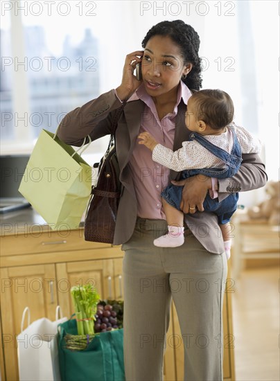 Mixed race mother holding baby and talking on cell phone