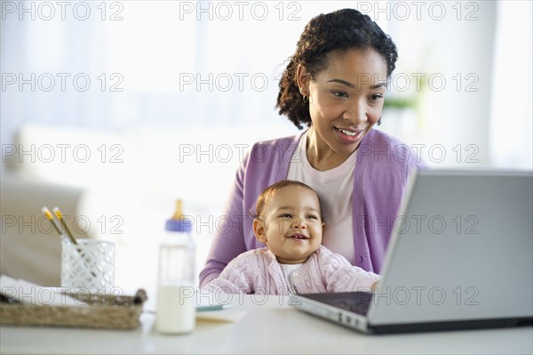 Mixed race woman holding baby and using laptop