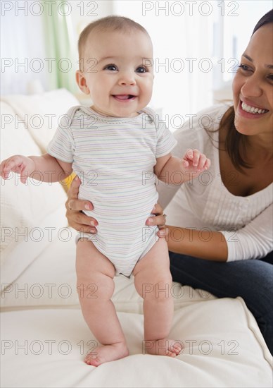 Mother supporting baby on sofa