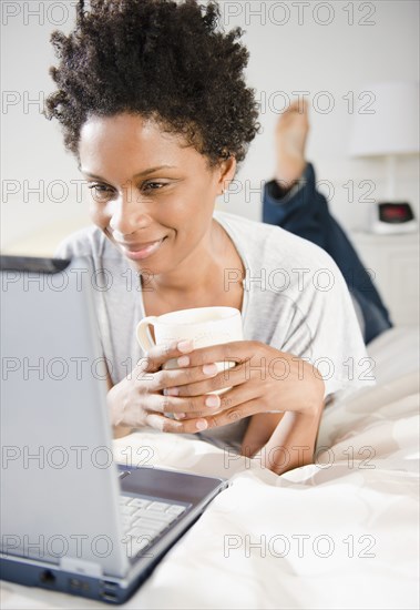 Black woman laying on bed using computer